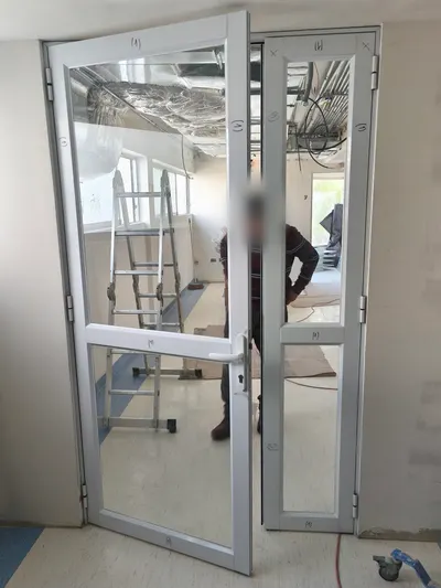 Puerta doble de aluminio blanco con cristal en un recinto en obra